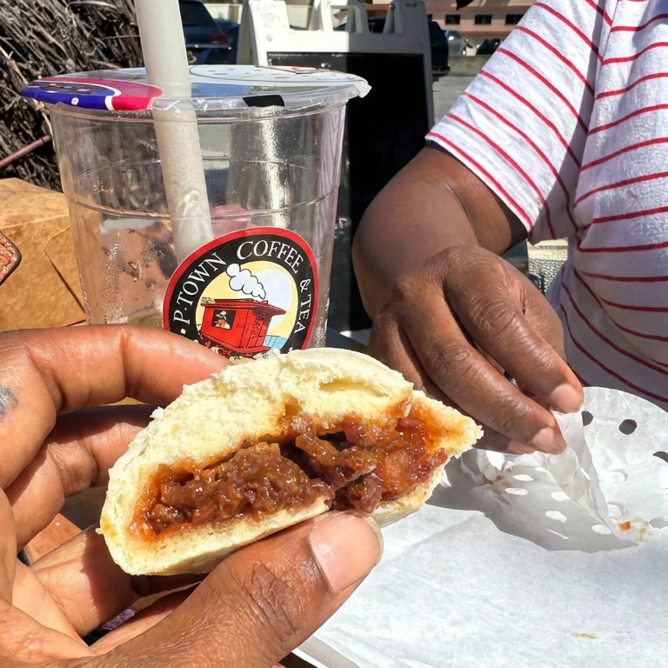 Hand holds a powdered pastry filled with fruit beside a Piton Coffee & Tea iced drink at an outdoor table.