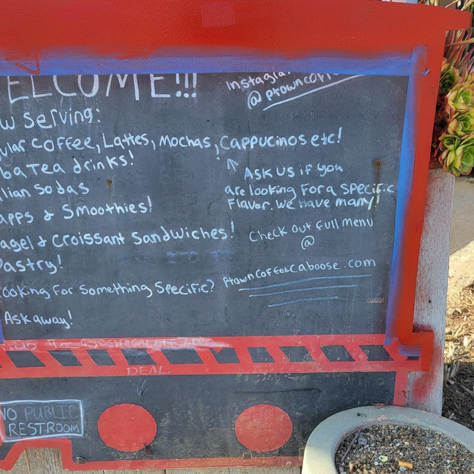 Red-framed chalkboard outside a café lists coffee, tea, smoothies, sandwiches, pastries, and social media information.